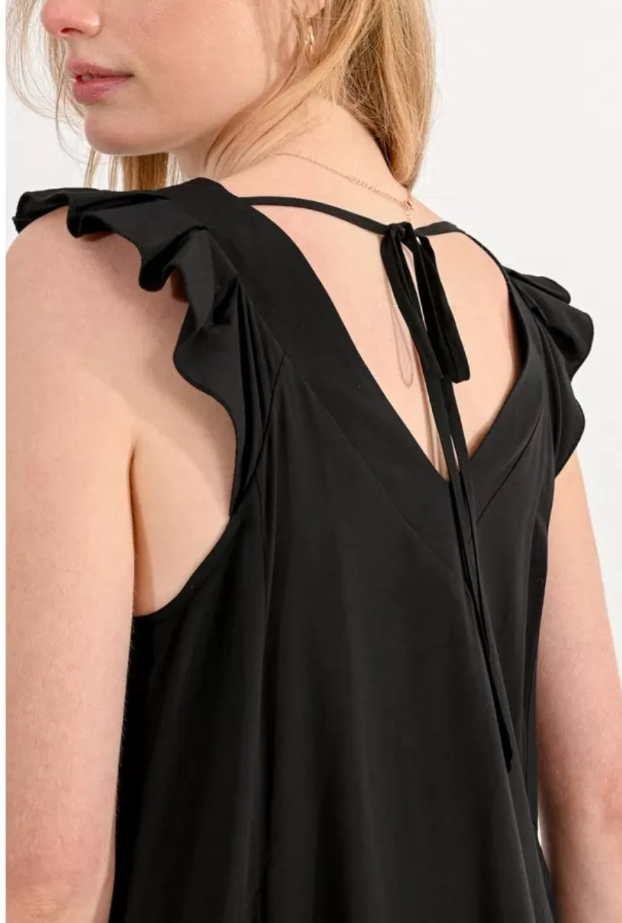 Femme blonde montrant les détails du dos et des manches de la robe noire débardeur aux bretelles  volantées, vue rapprochée.